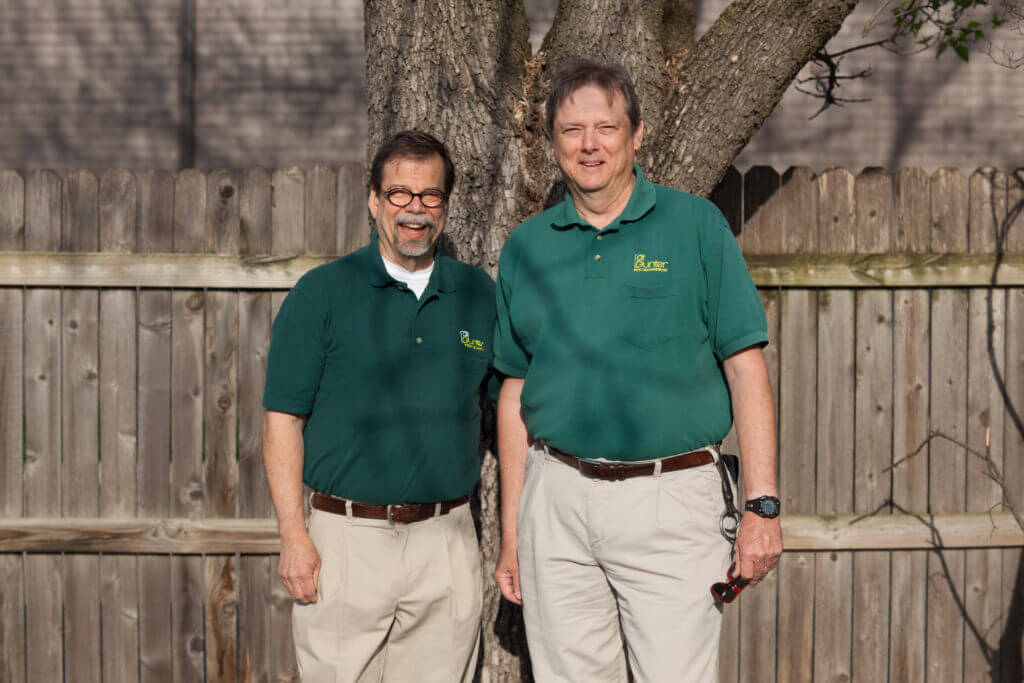 Two eco-friendly pest control employees standing in a backyard in green uniforms.