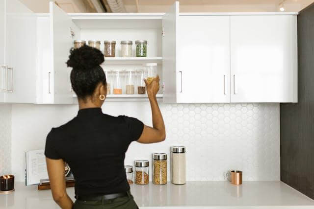 A woman taking a glass container out of the kitchen cabinet | Gunter Pest & Lawn A woman moving food items.